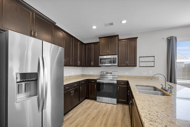 kitchen featuring sink, light stone counters, light hardwood / wood-style floors, stainless steel appliances, and dark brown cabinets