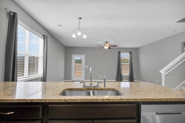 kitchen featuring sink, dark brown cabinets, pendant lighting, light stone countertops, and ceiling fan with notable chandelier