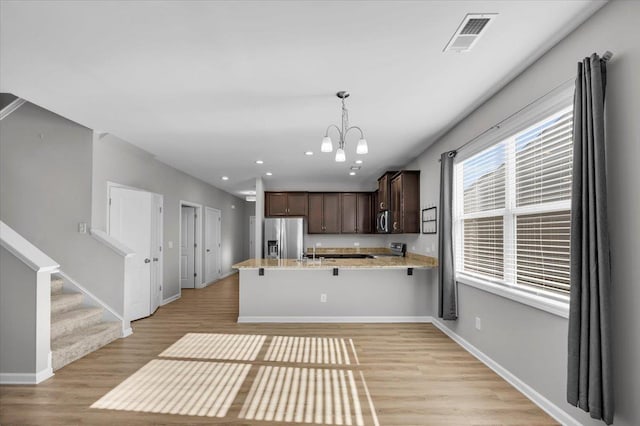 kitchen with pendant lighting, dark brown cabinetry, kitchen peninsula, stainless steel appliances, and light wood-type flooring