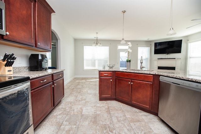 kitchen with appliances with stainless steel finishes, decorative light fixtures, sink, light stone countertops, and a healthy amount of sunlight