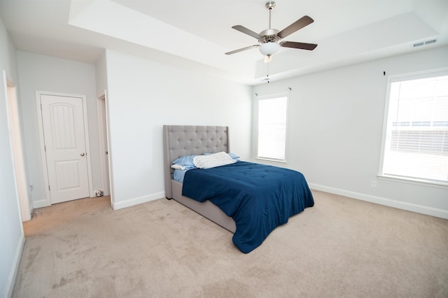 carpeted bedroom with ceiling fan, a tray ceiling, and multiple windows