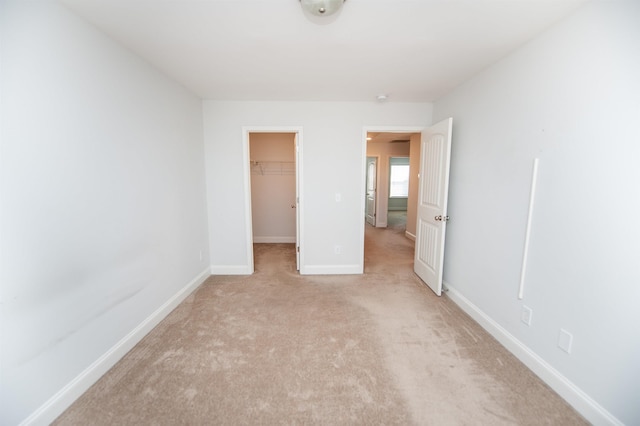 unfurnished bedroom featuring a walk in closet, light carpet, and a closet