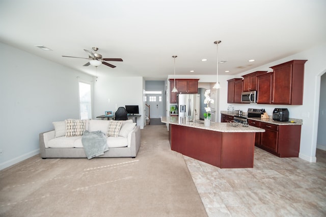 kitchen with ceiling fan, a kitchen island with sink, stainless steel appliances, light stone countertops, and decorative light fixtures