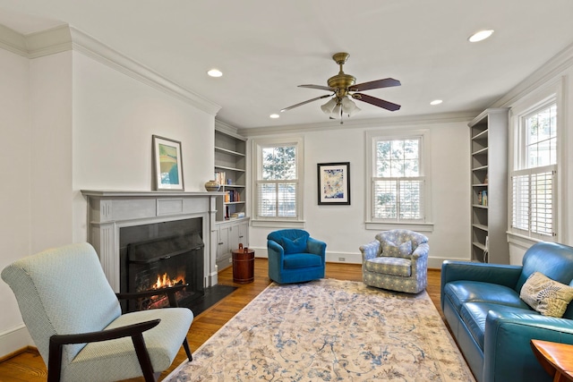 living room with hardwood / wood-style flooring, ceiling fan, ornamental molding, and built in shelves