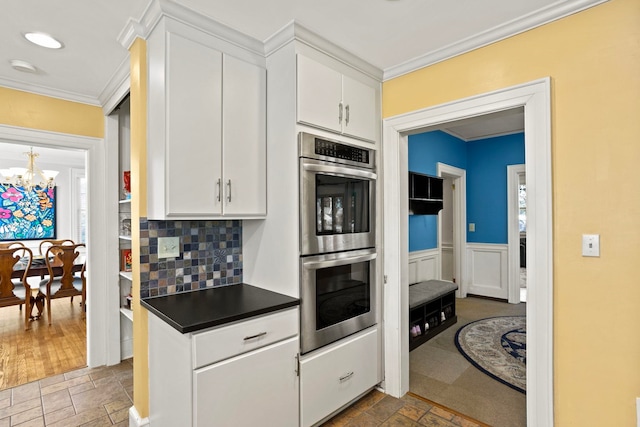 kitchen with crown molding, stainless steel double oven, white cabinets, and an inviting chandelier