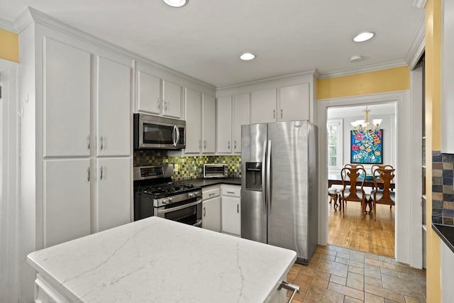 kitchen with tasteful backsplash, white cabinets, a notable chandelier, stainless steel appliances, and crown molding