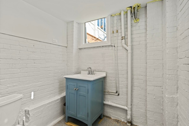 bathroom featuring vanity, toilet, and brick wall