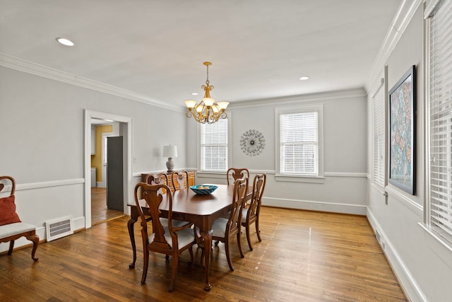 dining space with hardwood / wood-style flooring, crown molding, and a chandelier