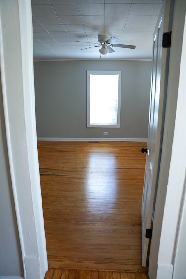 empty room with wood-type flooring, crown molding, and ceiling fan