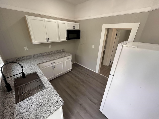 kitchen featuring white cabinetry, light stone counters, white refrigerator, dark hardwood / wood-style floors, and wooden walls