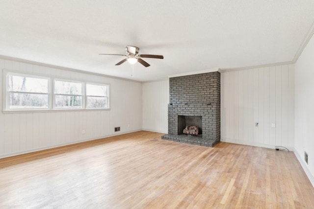 unfurnished living room featuring crown molding, ceiling fan, a brick fireplace, and light wood-type flooring