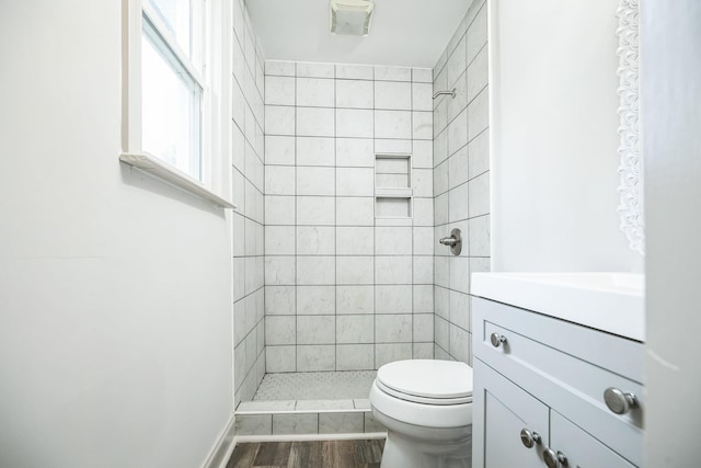 bathroom featuring a tile shower, vanity, hardwood / wood-style floors, and toilet