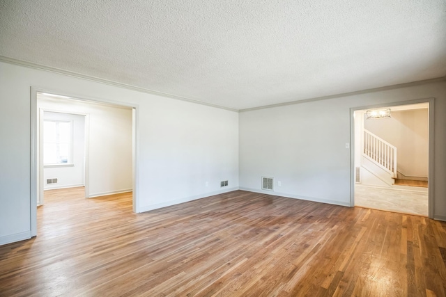 empty room with a notable chandelier, ornamental molding, a textured ceiling, and light hardwood / wood-style floors