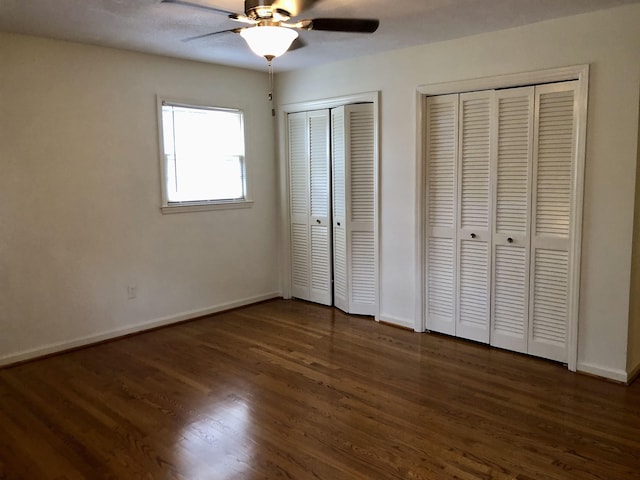 unfurnished bedroom with multiple closets, ceiling fan, and dark hardwood / wood-style floors