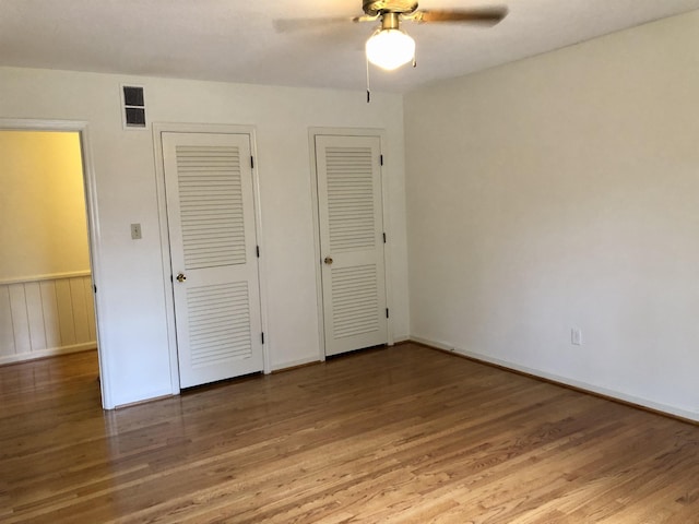 unfurnished bedroom featuring hardwood / wood-style flooring, two closets, and ceiling fan