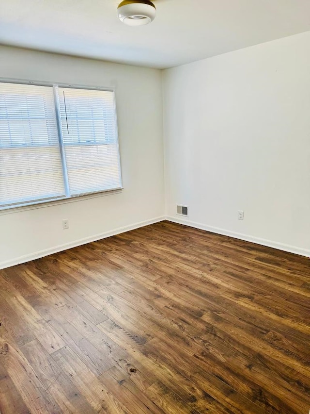 empty room with dark wood-type flooring, visible vents, and baseboards