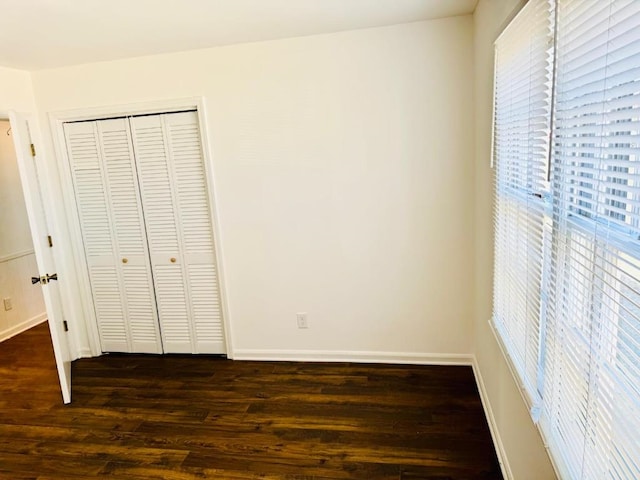 unfurnished bedroom featuring dark wood-style floors, a closet, and baseboards