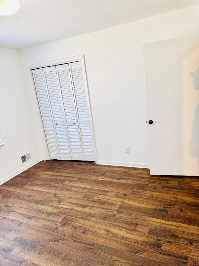 unfurnished bedroom with dark wood-style floors, a closet, visible vents, and baseboards