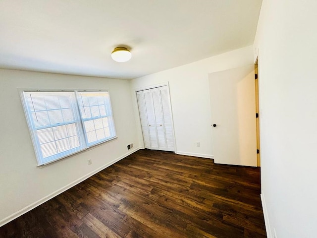 unfurnished bedroom featuring dark wood-style floors, visible vents, baseboards, and a closet