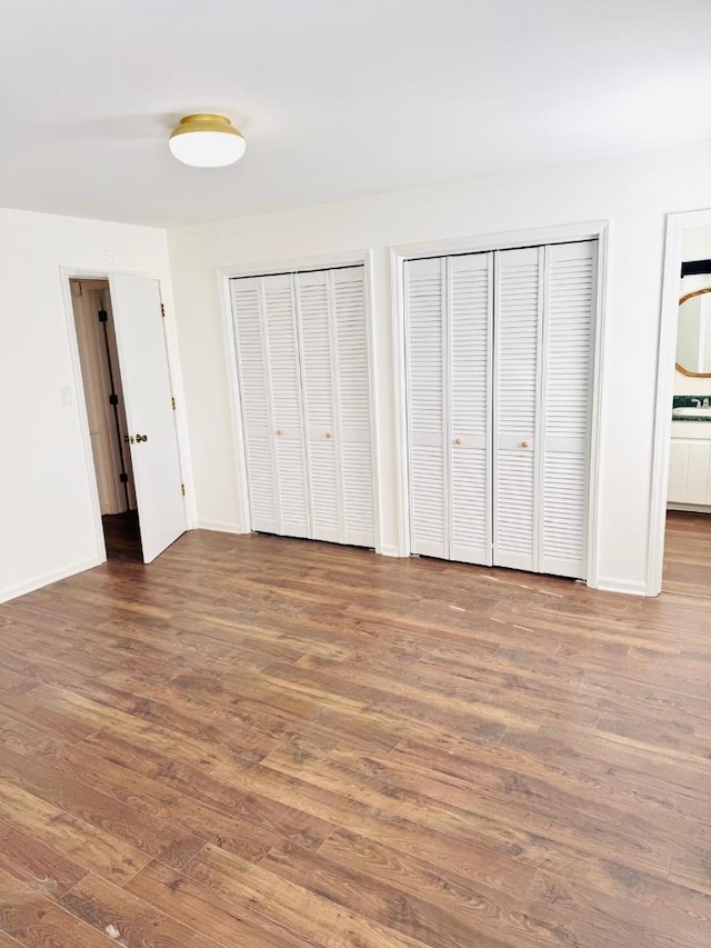 unfurnished bedroom with ensuite bath, baseboards, dark wood-type flooring, and two closets