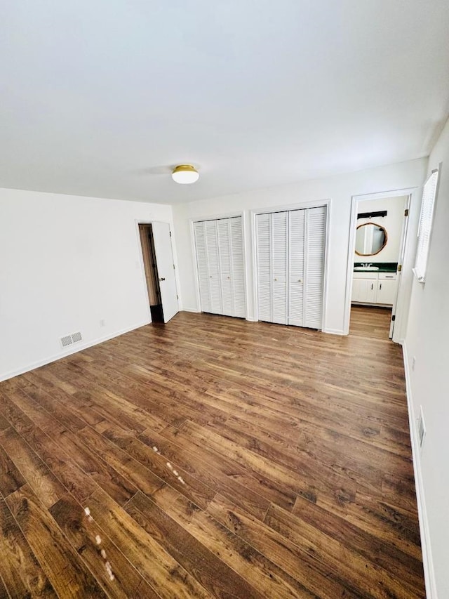 unfurnished bedroom with visible vents, dark wood-type flooring, and multiple closets