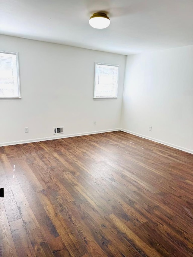 empty room featuring dark wood finished floors, visible vents, and baseboards