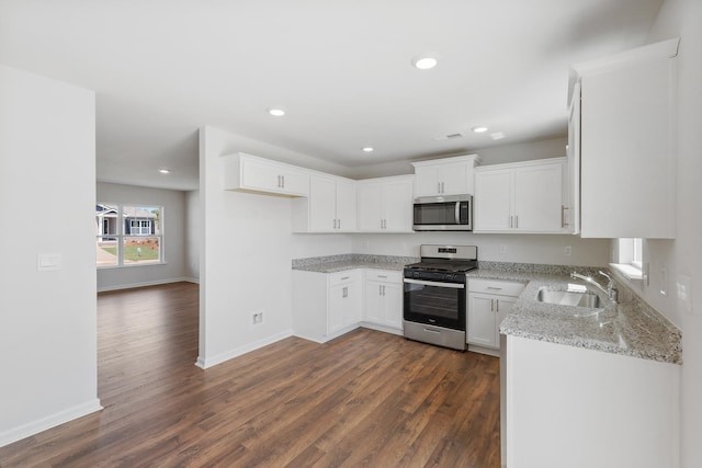 kitchen with sink, white cabinetry, stainless steel appliances, dark hardwood / wood-style floors, and light stone counters