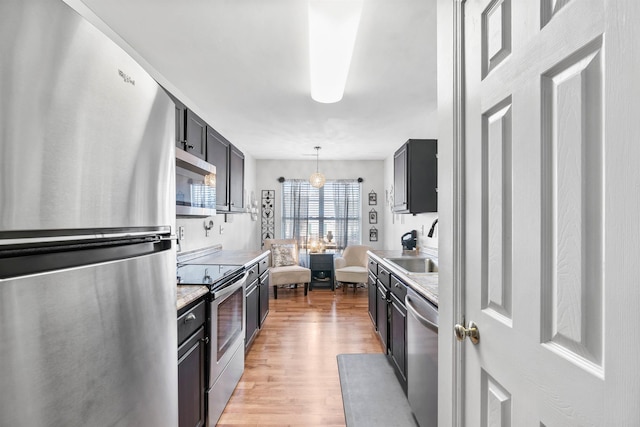 kitchen with pendant lighting, sink, light stone counters, stainless steel appliances, and light wood-type flooring