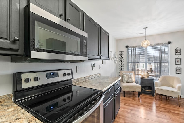 kitchen featuring hanging light fixtures, appliances with stainless steel finishes, light stone counters, and light hardwood / wood-style flooring