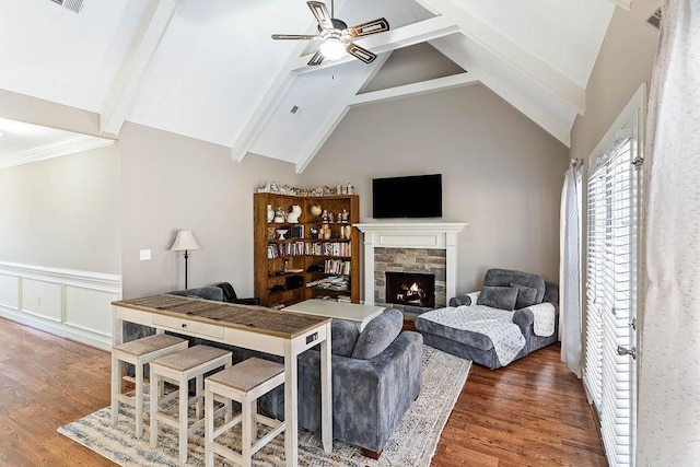 living room with a stone fireplace, dark hardwood / wood-style floors, vaulted ceiling with beams, and ceiling fan