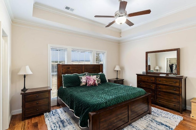 bedroom with hardwood / wood-style floors, ornamental molding, a raised ceiling, and ceiling fan