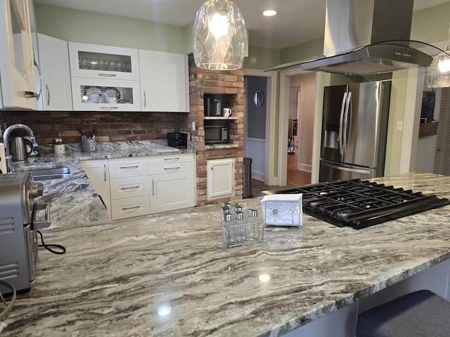 kitchen with sink, white cabinetry, decorative light fixtures, stainless steel fridge, and island exhaust hood