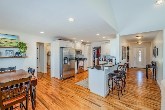 kitchen featuring stainless steel appliances, kitchen peninsula, white cabinets, and light wood-type flooring