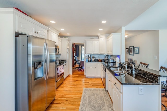 kitchen with sink, light hardwood / wood-style flooring, appliances with stainless steel finishes, white cabinetry, and a kitchen bar