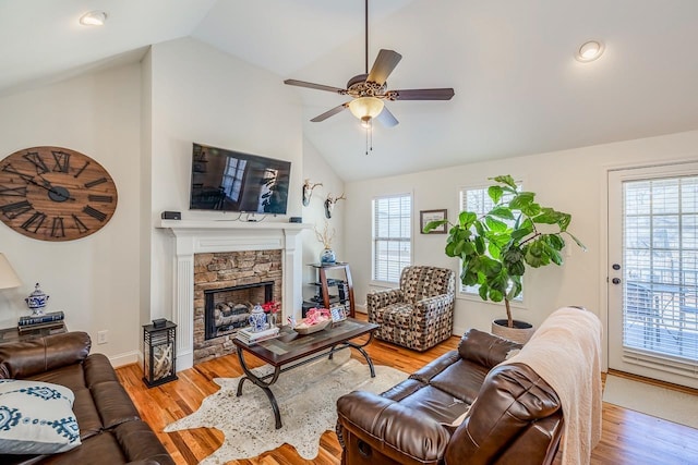 living room with lofted ceiling, a stone fireplace, light hardwood / wood-style floors, and ceiling fan