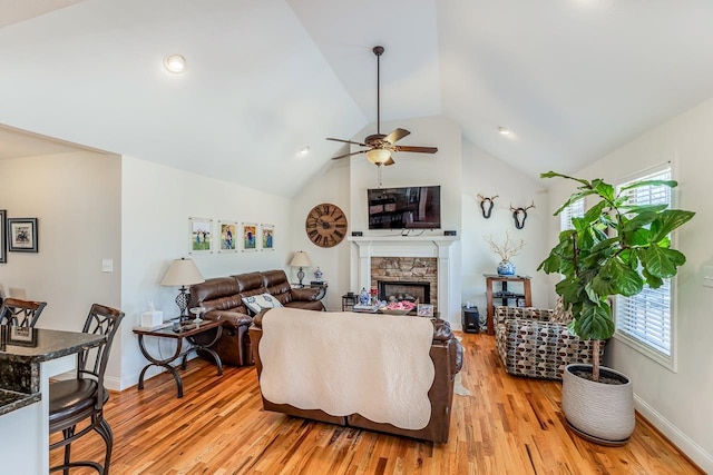 living room featuring ceiling fan, lofted ceiling, a stone fireplace, and light wood-type flooring