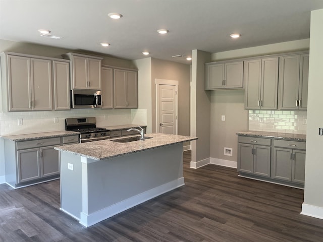 kitchen featuring gray cabinets, appliances with stainless steel finishes, sink, light stone counters, and a center island with sink