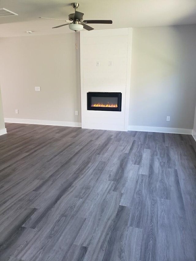 unfurnished living room featuring dark wood-type flooring and ceiling fan