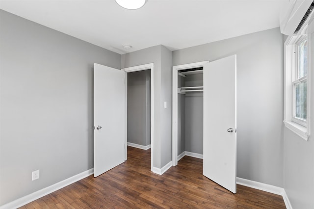 unfurnished bedroom with dark wood-type flooring, a wall unit AC, and a closet