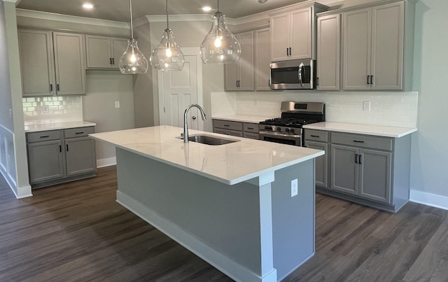 kitchen featuring pendant lighting, sink, stainless steel appliances, light stone counters, and a center island with sink