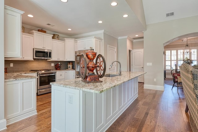 kitchen with sink, white cabinets, stainless steel appliances, light stone countertops, and a center island with sink