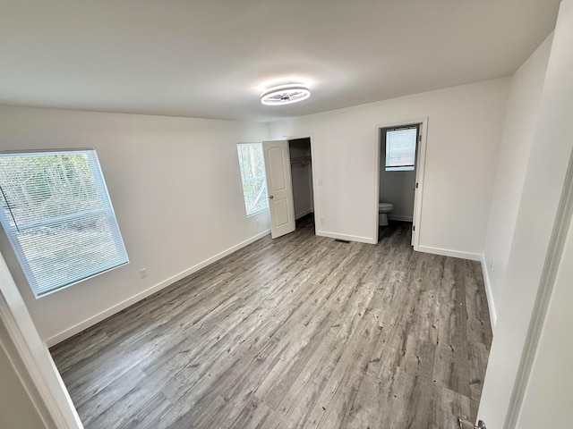 unfurnished bedroom featuring multiple windows, connected bathroom, a closet, and light hardwood / wood-style flooring