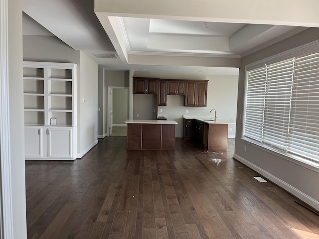 kitchen featuring sink, a center island, a tray ceiling, crown molding, and dark wood-type flooring