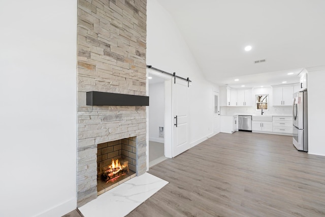 unfurnished living room with sink, hardwood / wood-style flooring, a stone fireplace, and a barn door