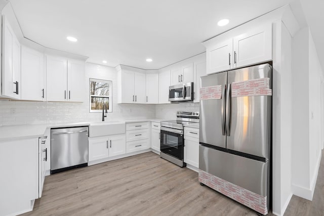 kitchen with sink, tasteful backsplash, light hardwood / wood-style flooring, appliances with stainless steel finishes, and white cabinets