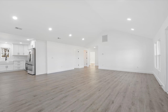 unfurnished living room with lofted ceiling, sink, and light hardwood / wood-style floors