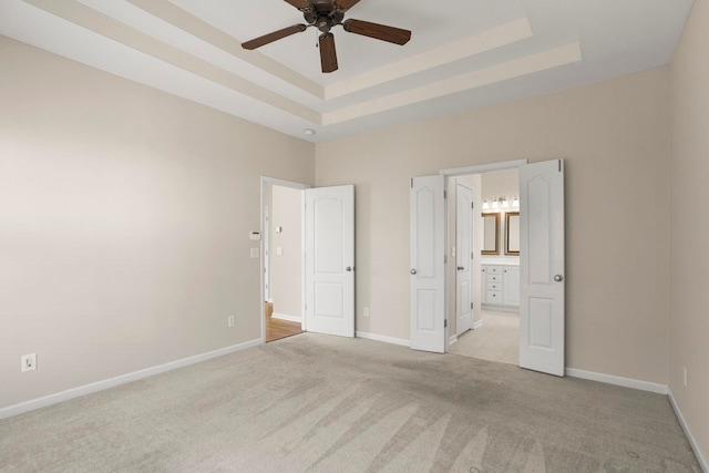 unfurnished bedroom featuring ceiling fan, ensuite bathroom, a tray ceiling, and light carpet