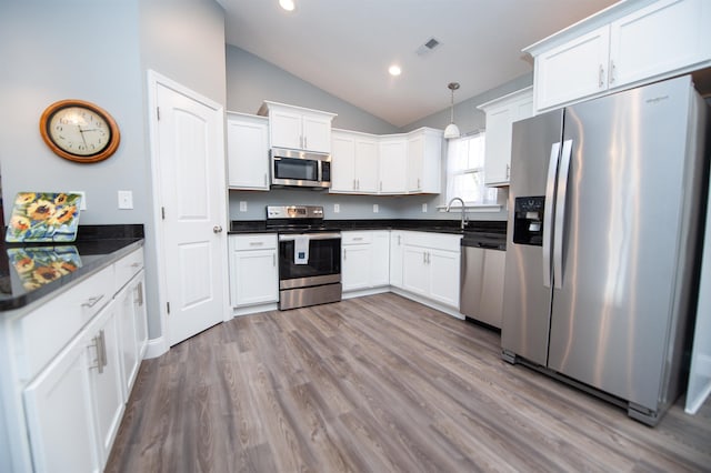 kitchen with stainless steel appliances, white cabinetry, hanging light fixtures, and vaulted ceiling