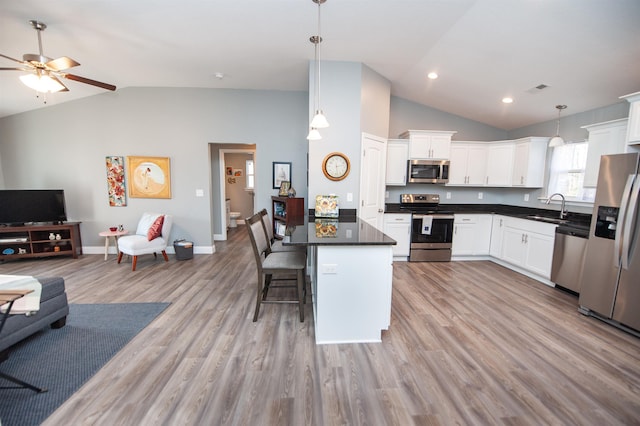 kitchen with appliances with stainless steel finishes, sink, white cabinets, a kitchen bar, and hanging light fixtures