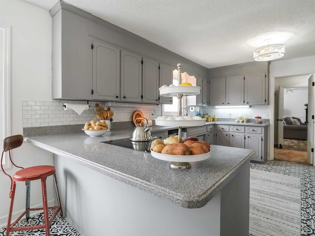 kitchen with a breakfast bar, gray cabinets, kitchen peninsula, and decorative backsplash